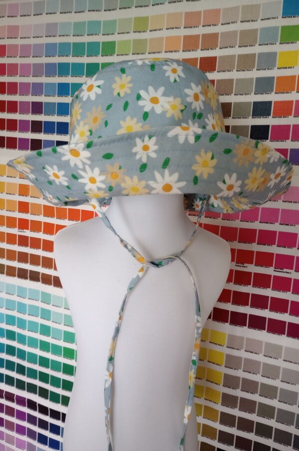 Mira hat blue daisy for kids is using daisy print on a light blue background. It is displayed on a mannequin at the front of color chart wall.