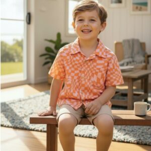 A boy sitting in the living room dressed in a beige shorts and checkered linen shirt with pink and orange twisted checkers, Kids Linen Shirt-Orange - by Miramara